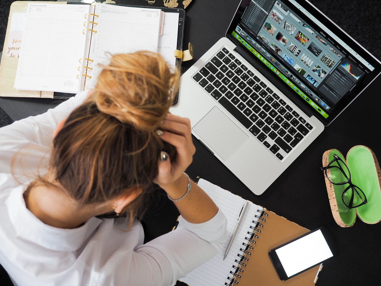 young woman hold her head in her hands over a desk with books and an open computer